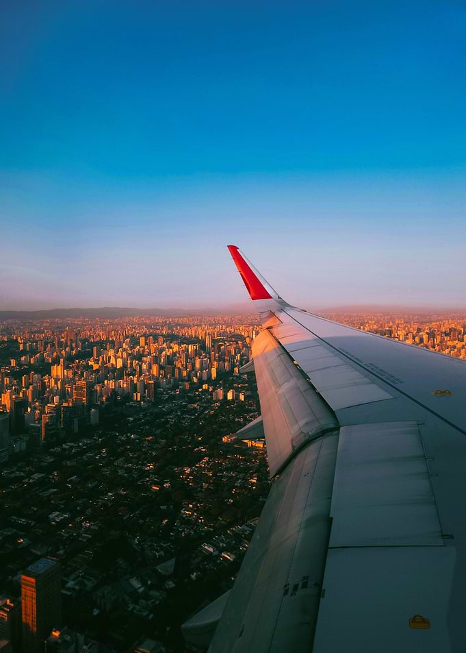 Airplane wing over city at sunset
