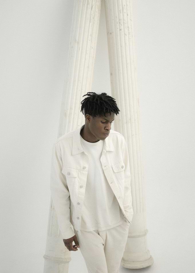 Daniel Caesar in White Outfit Poses by Columns