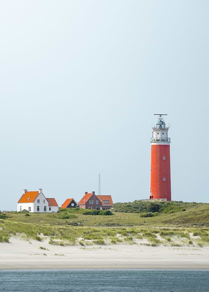 Red lighthouse on a grassy dune with houses