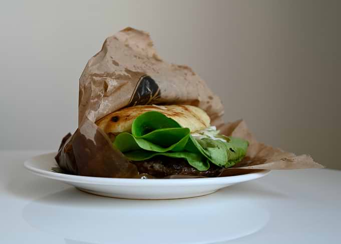 Burger wrapped in brown paper on a plate