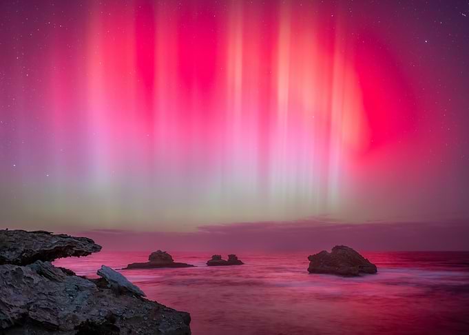 Vibrant Pink Aurora Over Ocean Rocks
