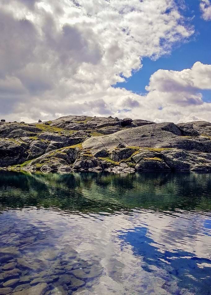 An Alpine Lake Reflecting a Blue Sky Veiled by Gray Summer Clouds