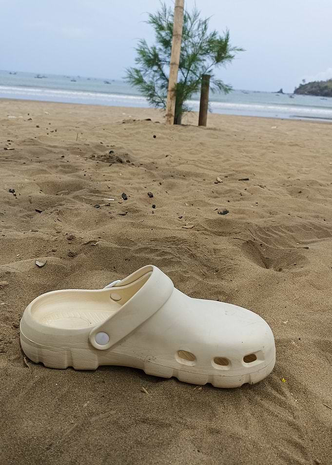 Single beige clog on sandy beach