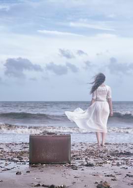 a woman is walking into the sea, leaving her luggage be ...