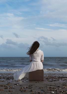 a woman sitting on a suitcase at the sea