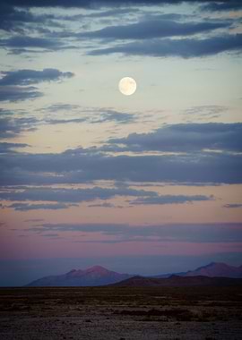 the moon rises over mountains in the desert.