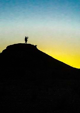 A photographer stands silhouetted on a hill as the dese ...