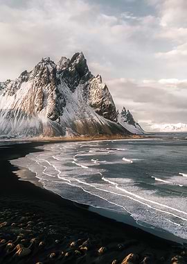 Snowy Mountain Range along the Icelandic Coast with black Sand Beach and Waves at Sunset