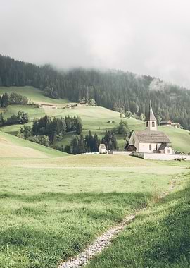 Dolomites, Italy I Mountain church in the heart of nature Alps landscape beside Lake Lago di Braies between green hills majestic fir trees and a mysterious mist with a dark moody aesthetic vibes