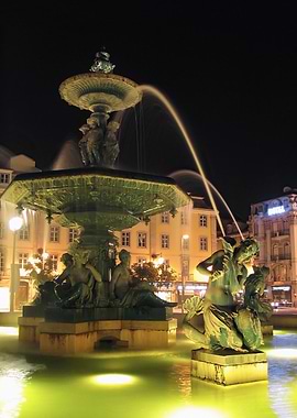 Illuminated bronze fountain by night with mermaid and water jets. Rossio Square, Lisbon, Portugal