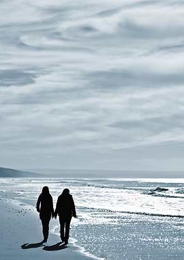 Silhouetted Lesbian Couple. Two Women Walk Side by Side Along a Sandy Beach Under a Calm Cloudy Sky.