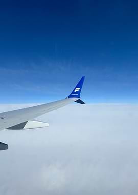 Airplane wing above clouds, blue sky