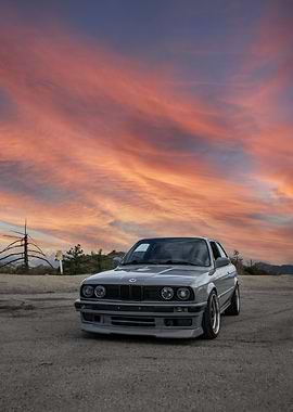 Gray BMW E30 under a sunset sky