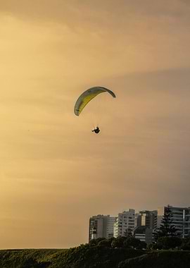 Paragliding over coastal city at sunset