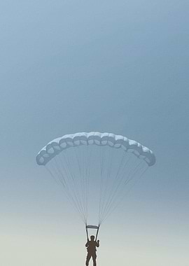 Parachutist descending under a white parachute