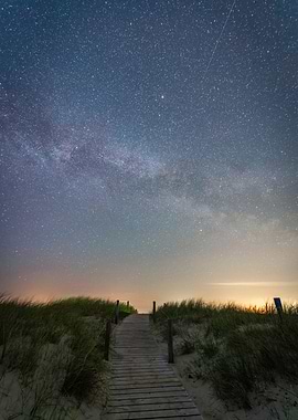 Starry milky way night sky with a shooting star over a pathway in the dunes