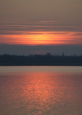 Sunset over a calm lake with a distant church spire