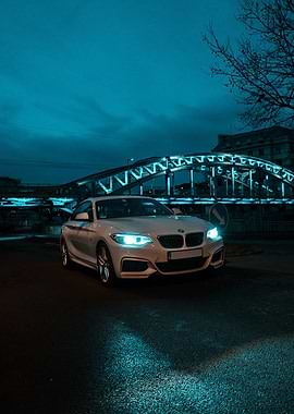 White BMW coupe at night under blue bridge lights