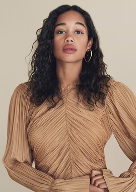 Laura Harrier in a pleated tan dress