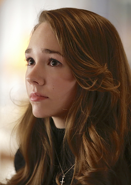 Holly Taylor with brown hair wearing a cross necklace