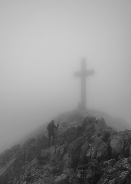 Hiker reaches mountain summit with cross in fog