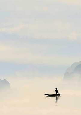 Fisherman on a boat in misty mountains