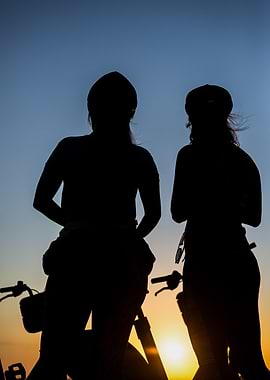 Silhouettes of two people with bicycles at sunset