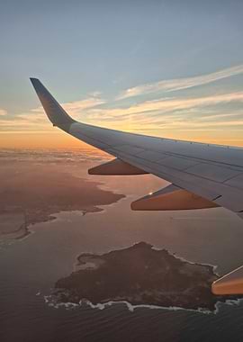 Airplane wing over coastal landscape at sunset