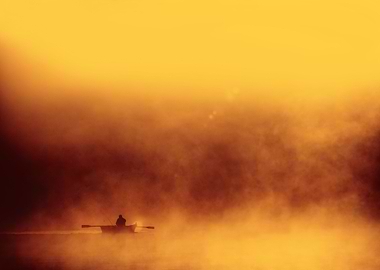 Lone fisher boat floating in foggy morning warm red yel ...
