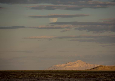 The moon rises over the desert mountains