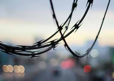 Photograph of a metal barb wire and a blurred urban lan ...