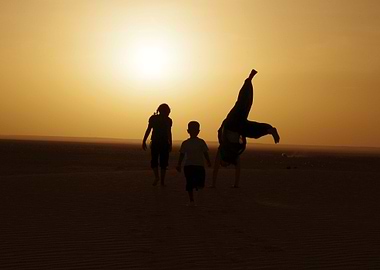 Sunset in the Sahara desert with children playing in th ...