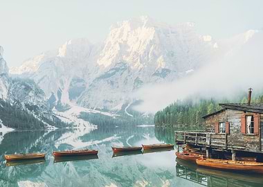 Dolomites, Italy I Lago di Braies lake with its wooden cabin and boats in front of the snow mountain from morning mist fog to the moody aesthetic atmosphere of sunrise pastel light in misty forest