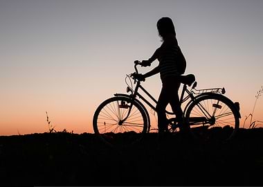 Silhouette of woman with bicycle at sunset