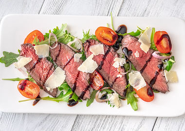 Italian beef tagliata salad with arugula and balsamic glaze on white plate