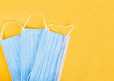 Three blue surgical masks on yellow