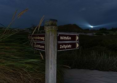 Signpost at night in the dunes with a Lighthouse in the background