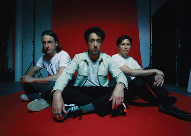 Three men sitting on red floor the wombats