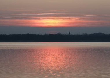 Sunset over a calm lake with a distant church spire