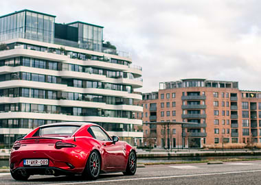 Red Mazda Miata parked by modern buildings